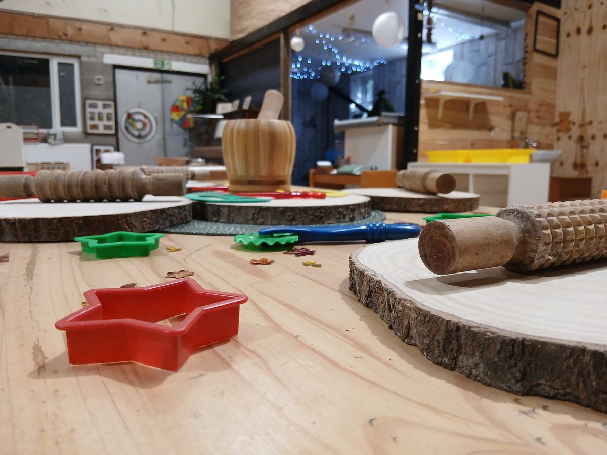 A wooden table set with wooden rolling pins, log slices, play dough cutters and a pestle and mortar