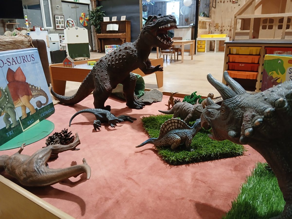 Toy dinosaurs on a small-world play table beside a dinosaur picture book