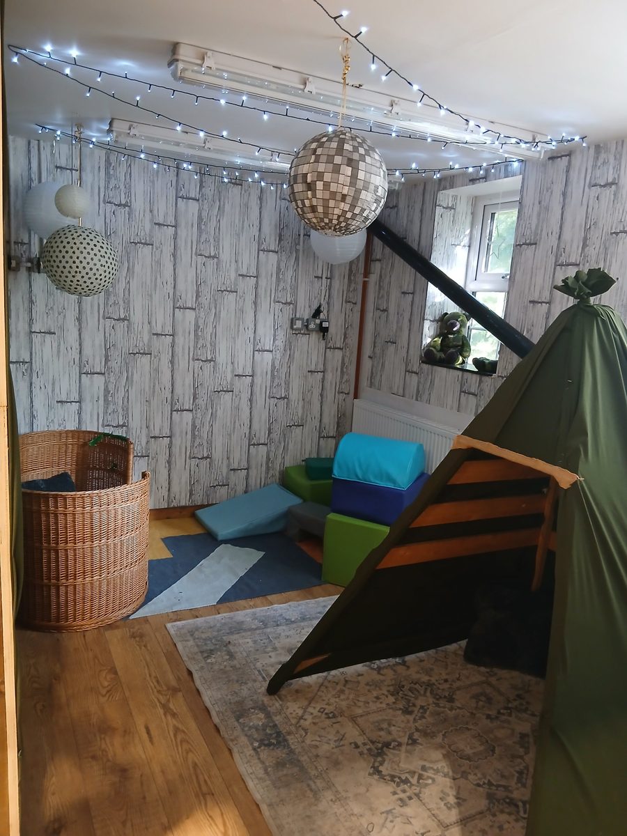 A quiet corner with soft foam blocks, a wicker basket, fairy lights and a green fabric den